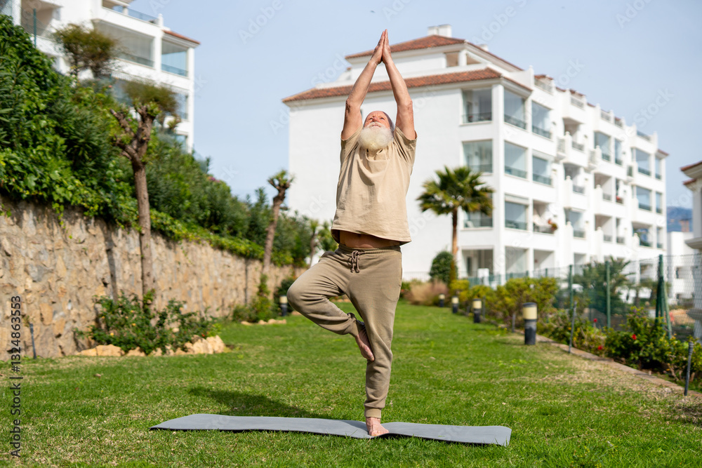 Fototapeta premium Senior man practicing yoga in the tree pose outdoors on a yoga mat