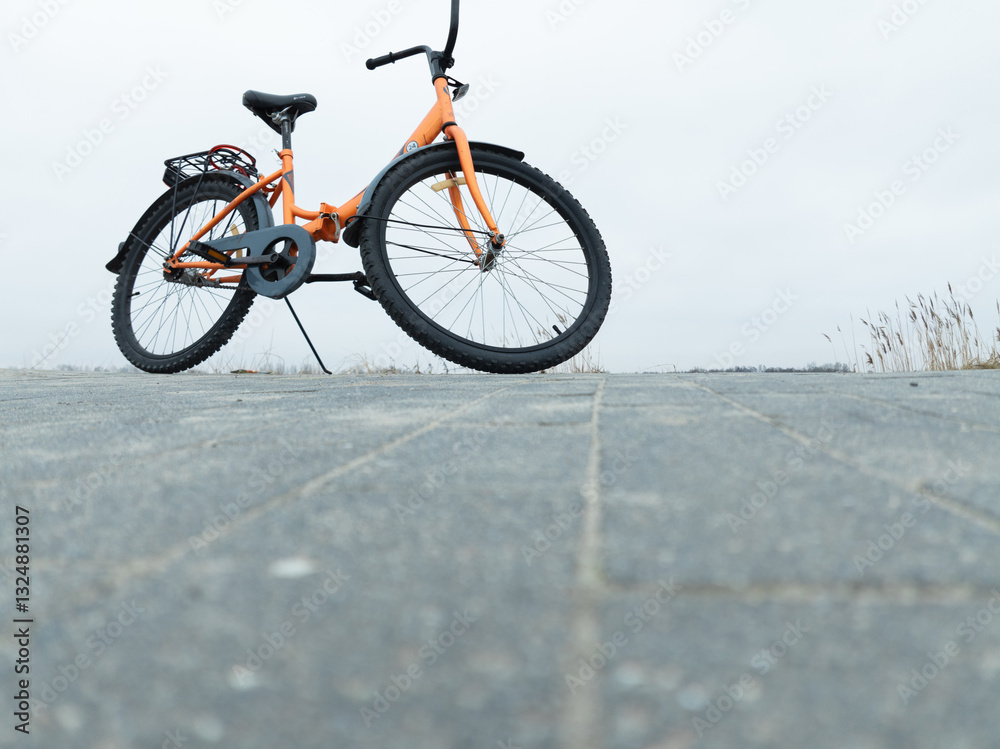 Fototapeta premium Orange Bicycle Parked on Gray Pavement Surrounded by a Foggy Landscape