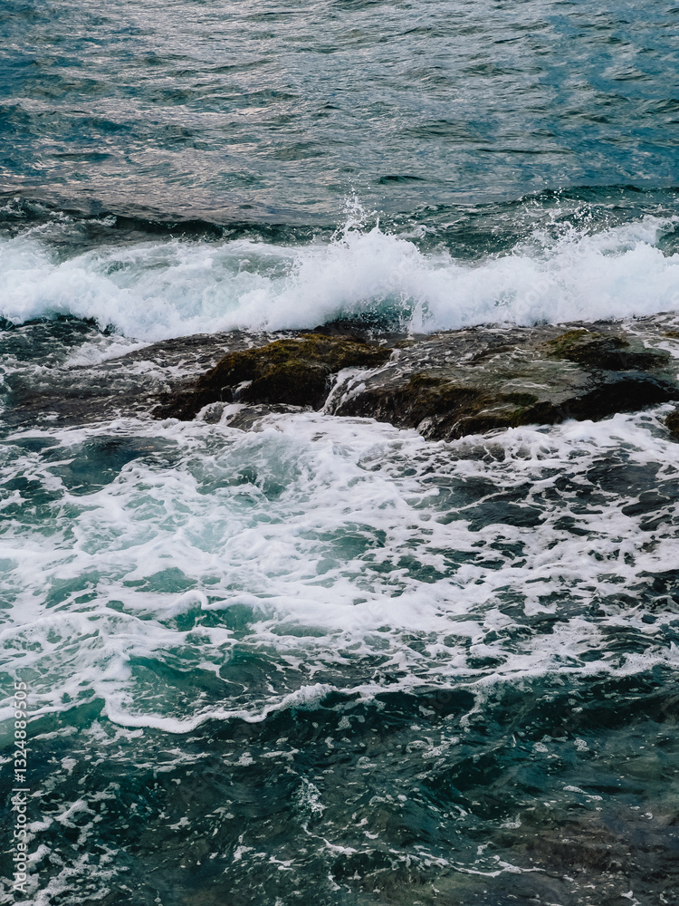 Fototapeta premium Ocean waves crashing against rugged rocks, creating dynamic splashes of white foam amidst vibrant turquoise waters in stunning seascape, raw beauty of nature. Powerful waves smashing rocky coastline