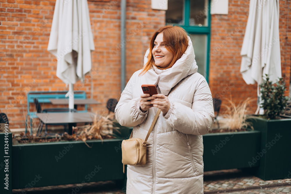 Young stylish 30s woman writes message on smartphone walking on city street. Urban lifestyle concept. Autumn time. Charming female wearing stylish outfit chatting online. High quality photo.