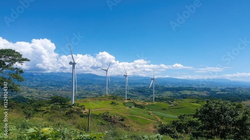 Massive wind turbines rotating on a green hilltop against a bright blue sky. photo