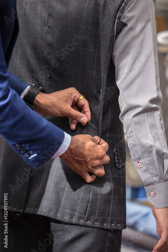 Close-up of bespoke tailor adjusting a dark gray pinstripe suit jacket on a client. Dressed in a blue suit, carefully buttons the jacket, showcasing the precision and craftsmanship