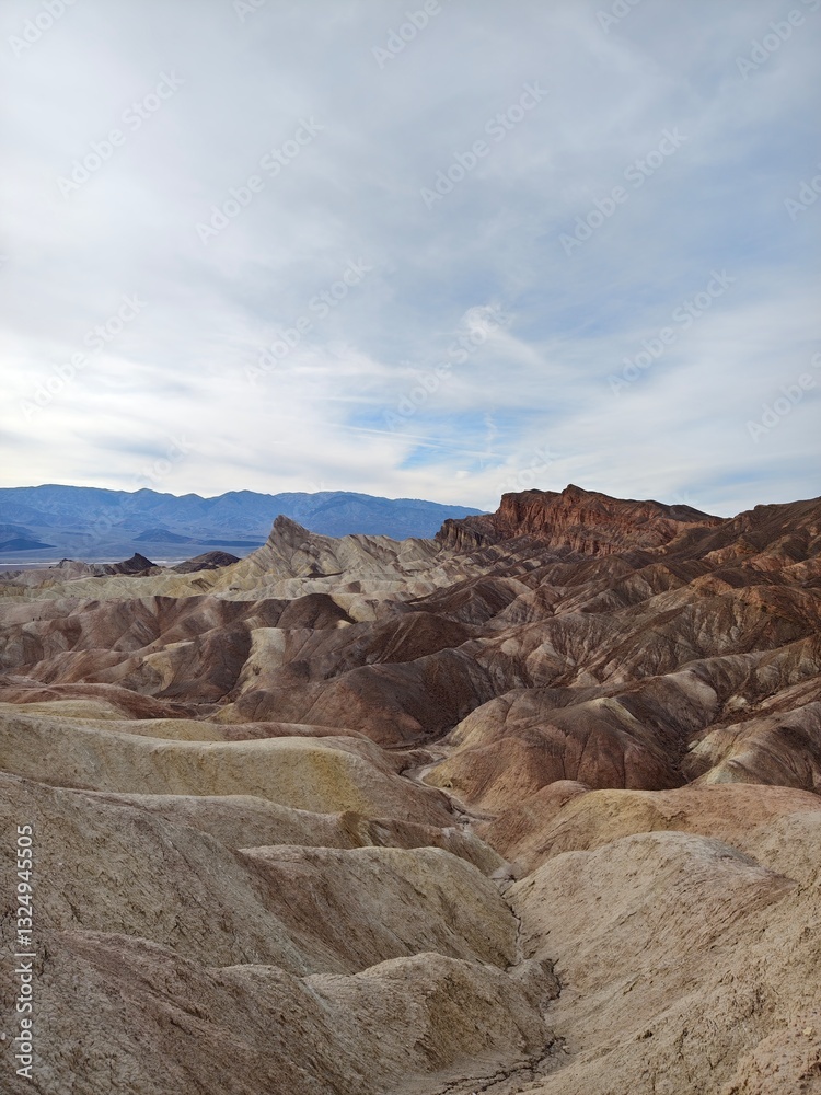 Fototapeta premium A sweeping view of undulating hills in earthy tones, leading to rugged peaks under a soft cloudy sky.