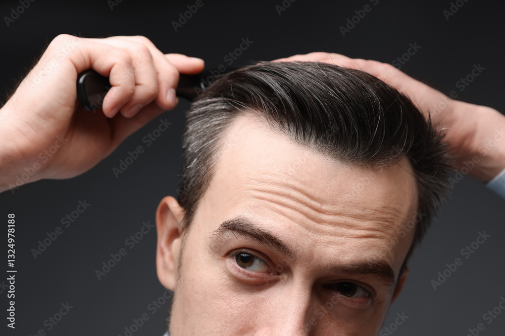 Obraz premium Handsome man combing his hair on dark background, closeup