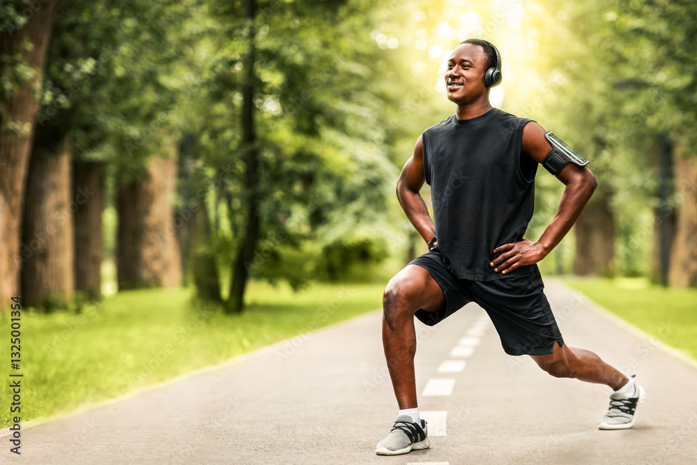Happy african american sportsman stretching legs, training at park, listening to music, blurred background, free space Happy african american sportsman stretching legs, training at park, listening to music, blurred background, free space