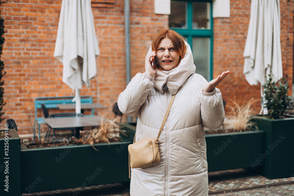 Angry woman on cell phone walking outside building. Frustrated woman talking on phone. Autumn time. Negative people emotion