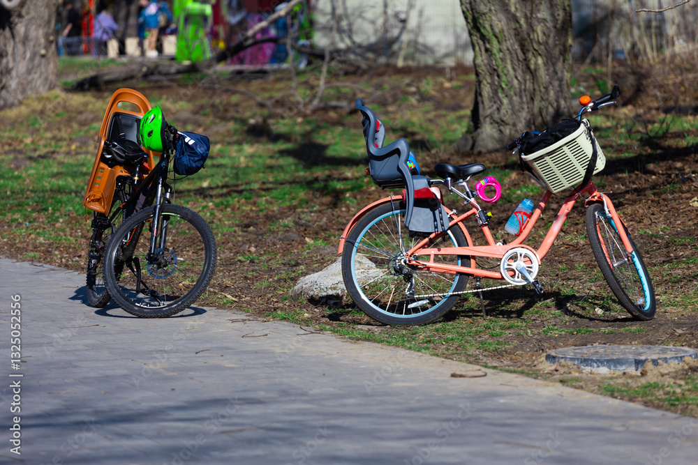Fototapeta premium Two Bicycles Parked Together in a Sunny Outdoor Setting, One Featuring a Child Seat, Showcasing a Family-Friendly Atmosphere in a Lush Green Park