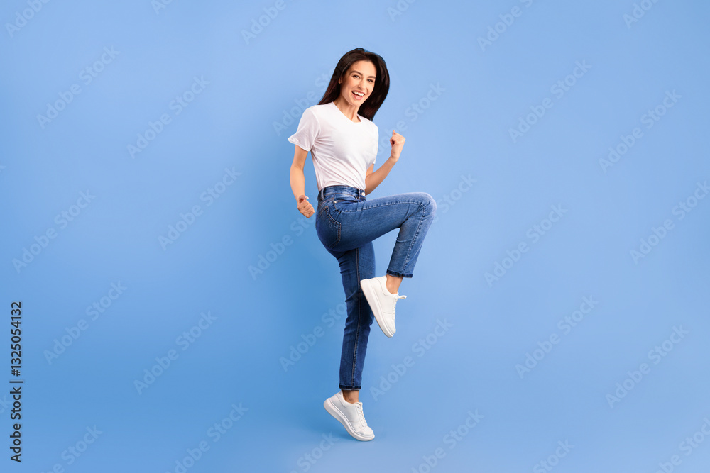 Funny portrait on joyful young woman jumping with clenched fists isolated on turquoise background, lifting one leg Funny portrait on joyful young woman jumping with clenched fists isolated on turquoise background, lifting one leg