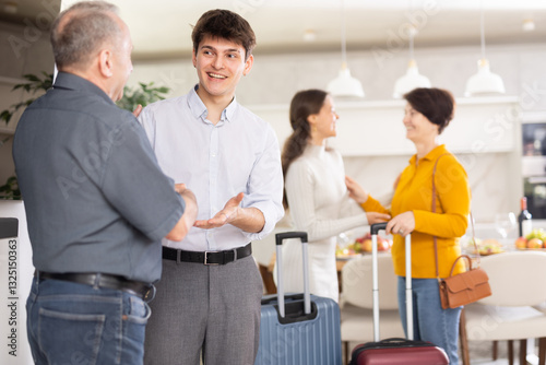 In gesture of familial affection, hospitable son-in-law greeting visiting elderly father-in-law with handshake, embodying warm welcome in comfy home setting....