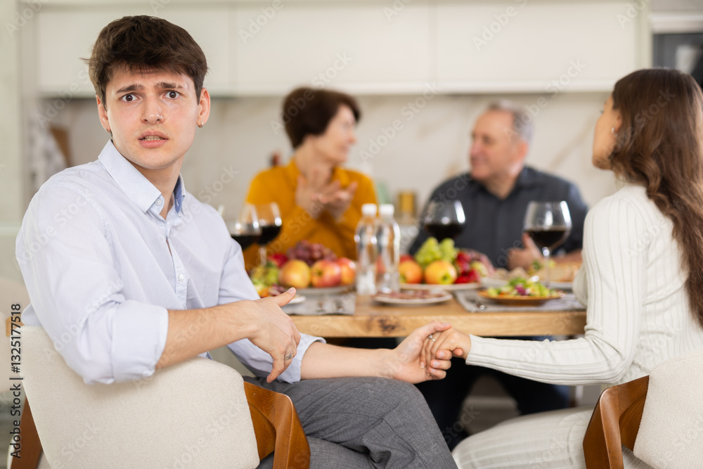 Upset young guy at family holiday table with parents at home. Unpleasant discussion Upset young guy at family holiday table with parents at home. Unpleasant discussion