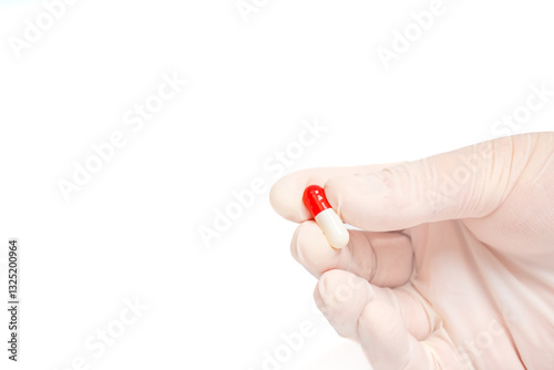 Gloved hand holding a red capsule on isolated white background. Medicine, health, treatment and pharmaceutical concept. Close up of hand fingers with a single pill. Copy space