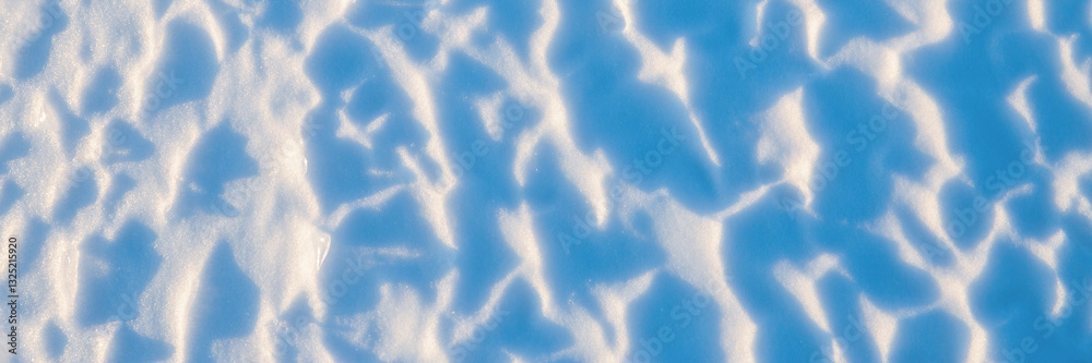 Beautiful winter background with snowy ground. Natural snow texture. Wind sculpted patterns on snow surface. Wide panoramic texture for background and design.