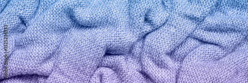 A soft and textured gradient blue and purple knitted fabric with gentle waves and folds, creating a cozy and warm appearance. Ideal for textile backgrounds, fashion, or home decor themes.