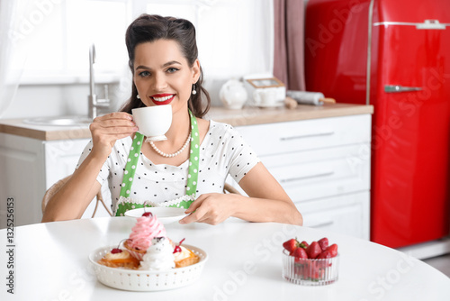 Portrait of beautiful pin-up woman with cup of coffee and sweets in kitchen