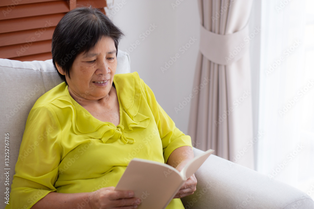Asian senior woman reading a book sitting on sofa with relax in living room at home, elderly woman reading literature on couch with cozy, hobby and recreation in weekend, lifestyles concept. Asian senior woman reading a book sitting on sofa with relax in living room at home, elderly woman reading literature on couch with cozy, hobby and recreation in weekend, lifestyles concept.