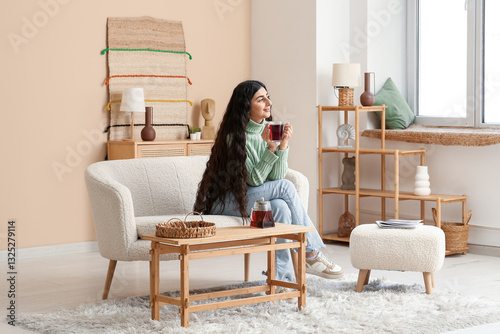Relaxed young woman enjoying hot tea on cozy sofa in modern living room inter...