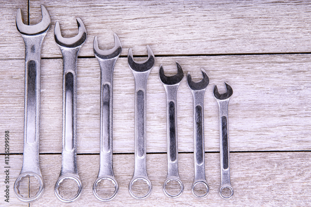 Set of metallic wrenches arranged in size order on a rustic wooden background. Ideal for themes related to mechanics, construction, DIY projects, and professional toolkits in industrial settings.