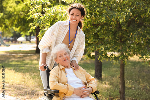 Young African-American female medical worker walking with elderly woman on wheelchair outdoors
