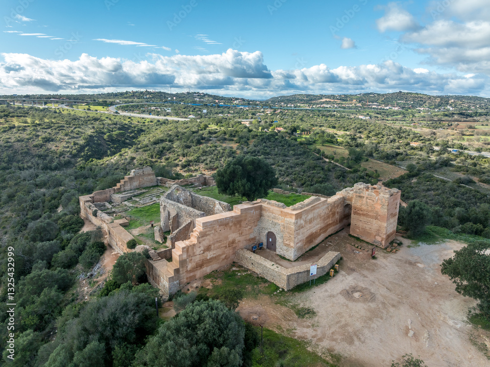 Stone ramparts & crenellated walls define Paderne Castle's medieval architecture, a historic Portuguese fortress against a blue sky