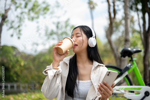 Photography An asian woman is sipping a drink while holding smartphone, sitting and chilling in park or garden