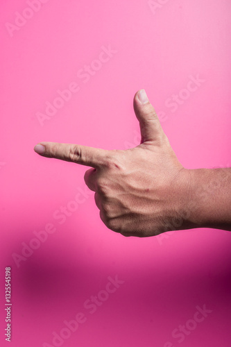 Human hand in finger gun gesture with thumb raised and index finger extended, mimicking a pistol shape on a vibrant pink background, symbolizing creativity, play, or expression in bold style.