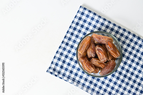 Top view of kurma tunisia or sweet dried dates palm fruits in a little glass bowl with napkin on below. Isolated on white background. clipping path. Flat lay. Empty space, copy space, free space. photo