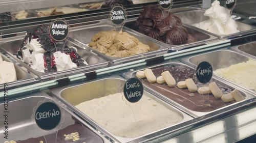 Slide shot of multiple metal boxes with ice cream flavours displayed under glass counter. Gelateria concept