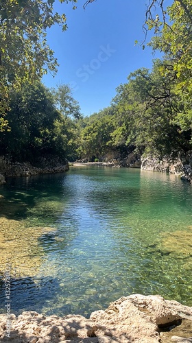Serene crystal-clear river pool in a lush green canyon under a vibrant blue sky.