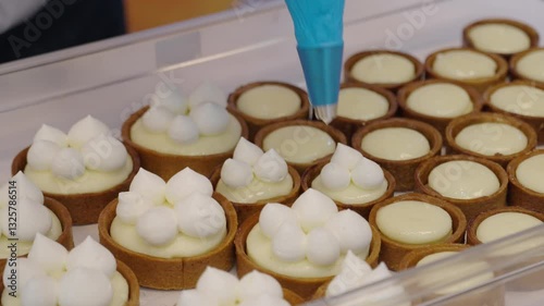 Confectioner decorating cakes with fresh cream from confectionary bag close up