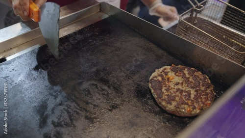 Person flipping meat cutlet on frying pad with spatula close up