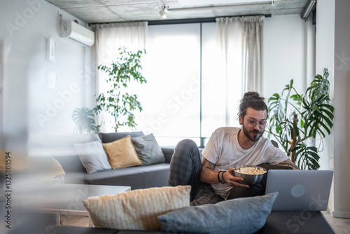 Freelancer working from home watching movie on laptop and eating popcorn