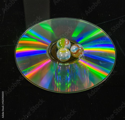 Rainbow colors reflected on a compact CD, three glass balls in the center of CD.