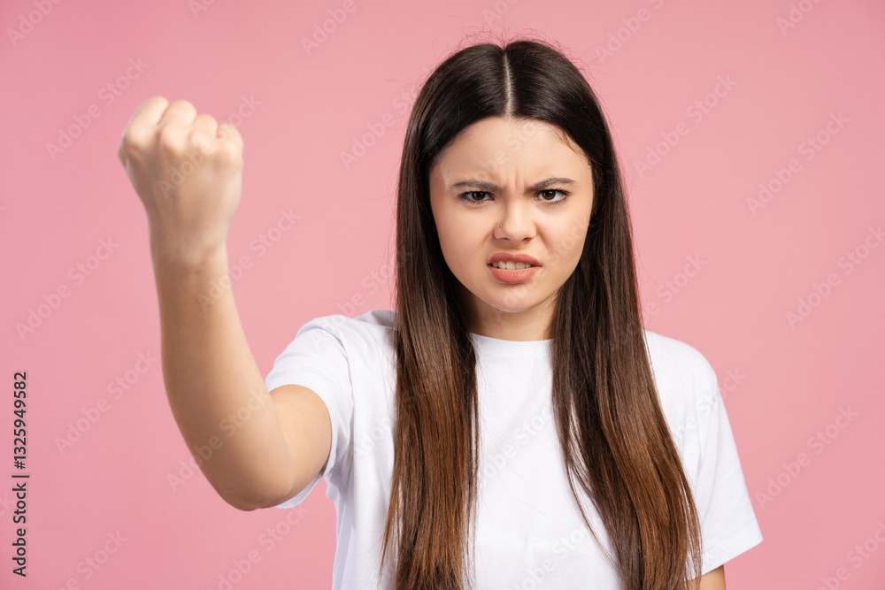 Angry girl showing clenched fist and angry expression on pink background Angry girl showing clenched fist and angry expression on pink background