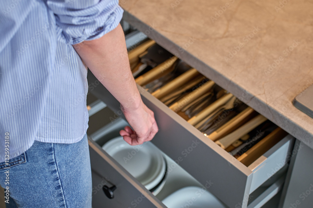 Person opens a kitchen drawer with various utensils in wooden cutlery tray. Woman opening kitchen cabinet. Concept of home organization and functionality interior