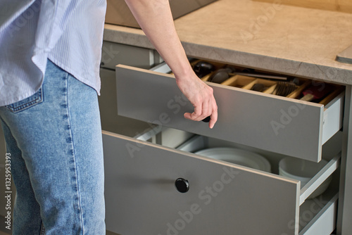 Person opens a kitchen drawer with various utensils in wooden cutlery tray. Woman opening kitchen cabinet. Concept of home organization and functionality interior