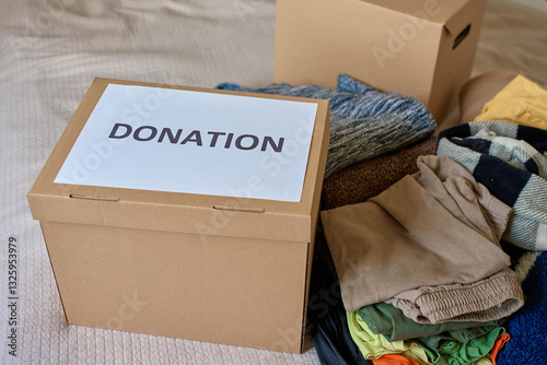Obraz na płótnie Used clothes near cardboard box labeled Donation at home. Concept of charity, kindness and social responsibility w salonie