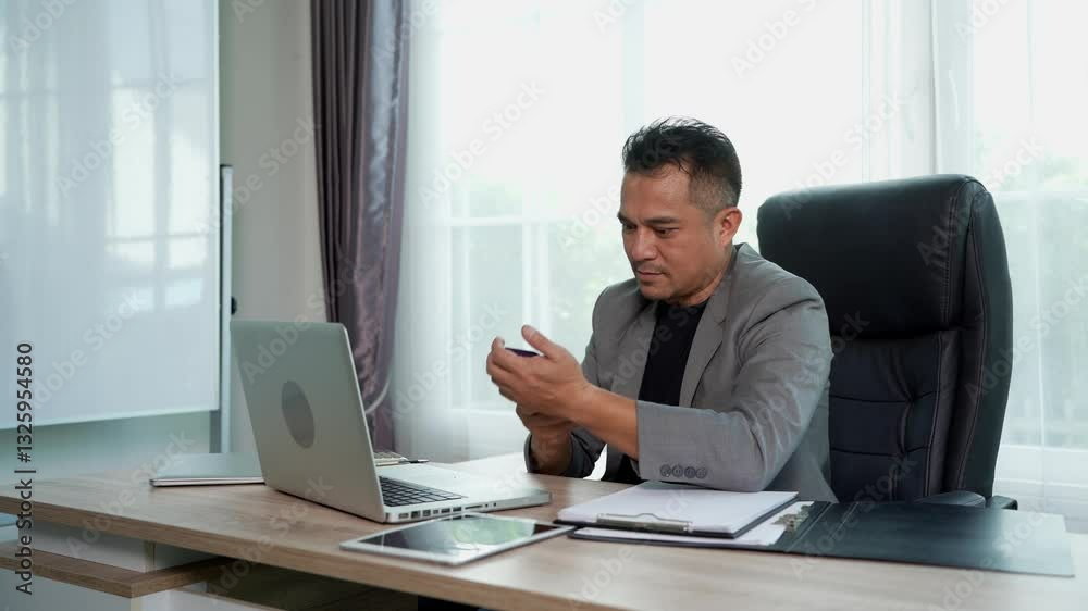 Professional businessman in gray blazer working on laptop computer, He concentrate his work, typing on laptop and talking on smartphone while working at a desk in modern office Professional businessman in gray blazer working on laptop computer, He concentrate his work, typing on laptop and talking on smartphone while working at a desk in modern office