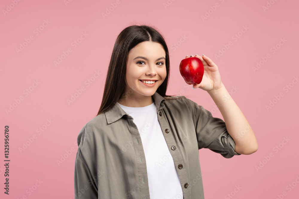 Young, smiling girl showing red apple and smiling on pink background Young, smiling girl showing red apple and smiling on pink background