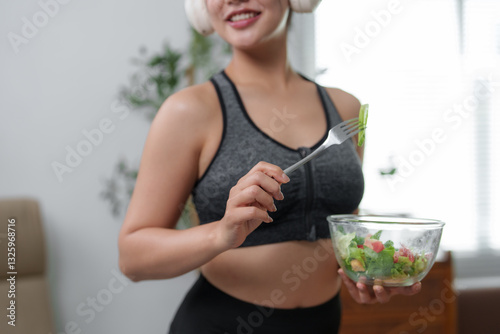 Smiling sportswoman eating fresh salad at home photo