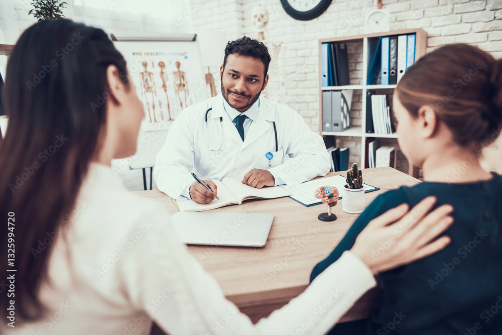 Fototapeta premium Indian doctor seeing patients in office. Doctor is taking notes listening to mother and daughter.