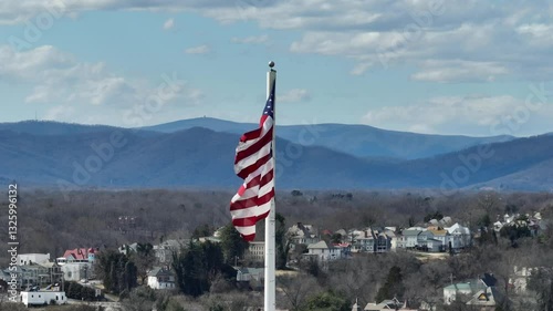 American flag on flagpole waving in wind during sunny day. Housing and homes in Background. Mountain silhouette in distance. Aerial wide shot.