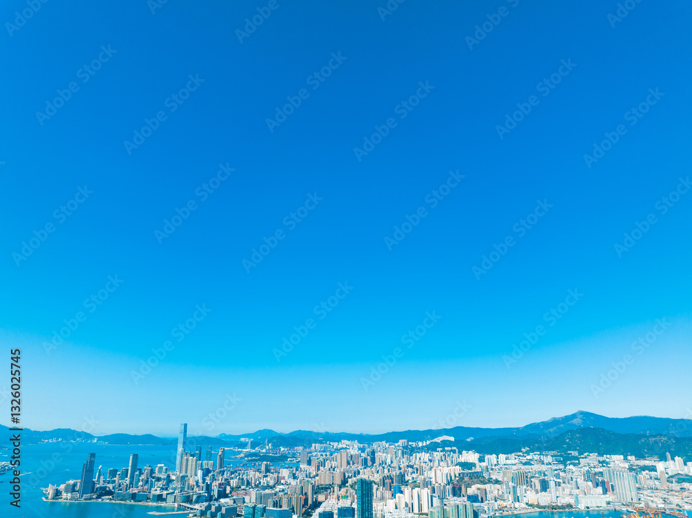 Obraz premium Aerial panorama of Hong Kong city with skyscrapers and mountains under a clear blue sky, showcasing a stunning cityscape view.