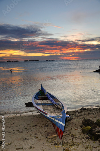 Traditional sailing and rowing fisherman boat. Dramatic gold sunset sky background