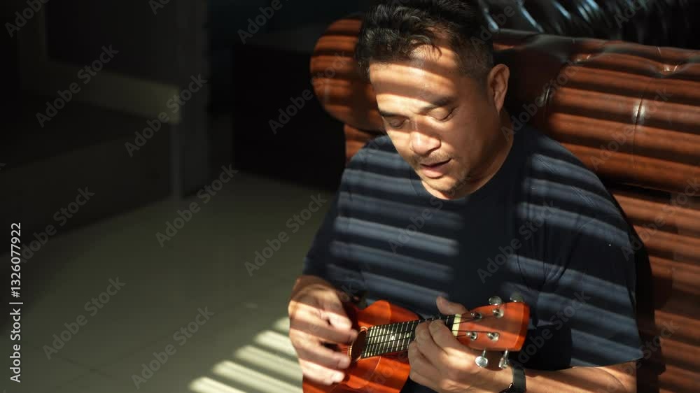 Locked medium shot, Asian middle-aged man sits Leaning Against Brick Wall and Enjoy to playing Ukulele at home, Attractive composer man who working with music