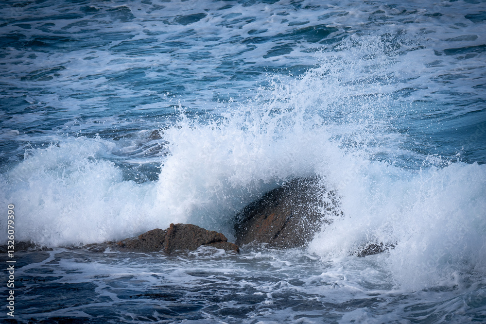 Fototapeta premium A powerful ocean wave crashing against coastal rocks, sending white spray into the air