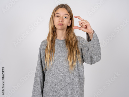 beautiful caucasian girl wearing grey track-suit  purses lip and gestures with hand, shows something very little.