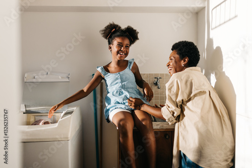 фотографія Happy mother and daughter doing laundry with a machine at home