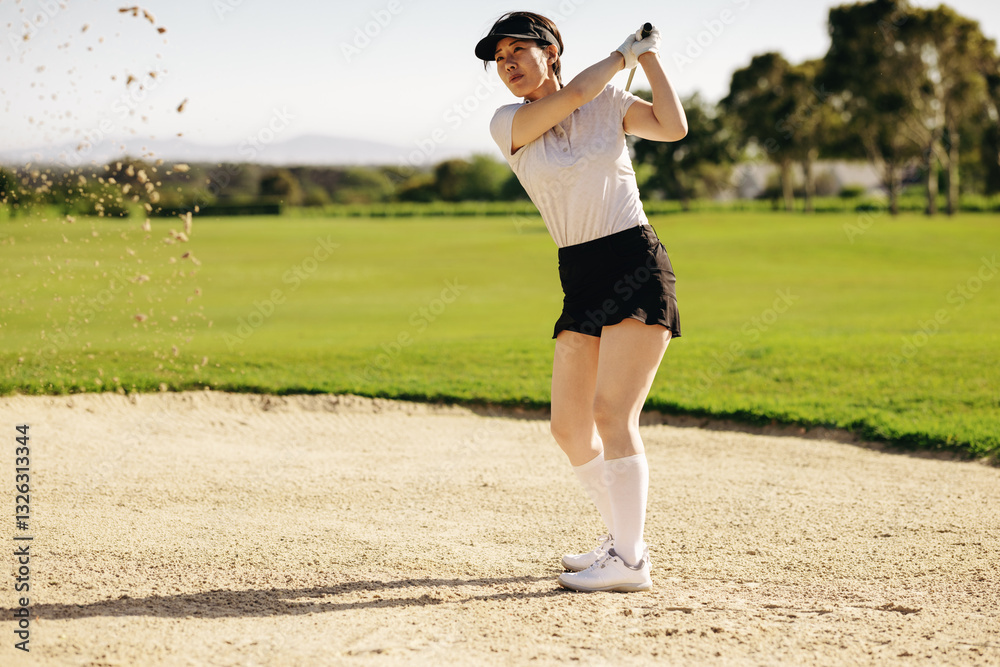 Fototapeta premium Active woman showcasing her golf swing in a sand bunker on a warm, sunny day