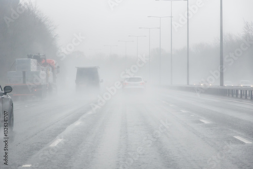A rainy motorway scene with vehicles driving through dense mist and spray, reducing visibility and creating a hazy atmosphere in England
