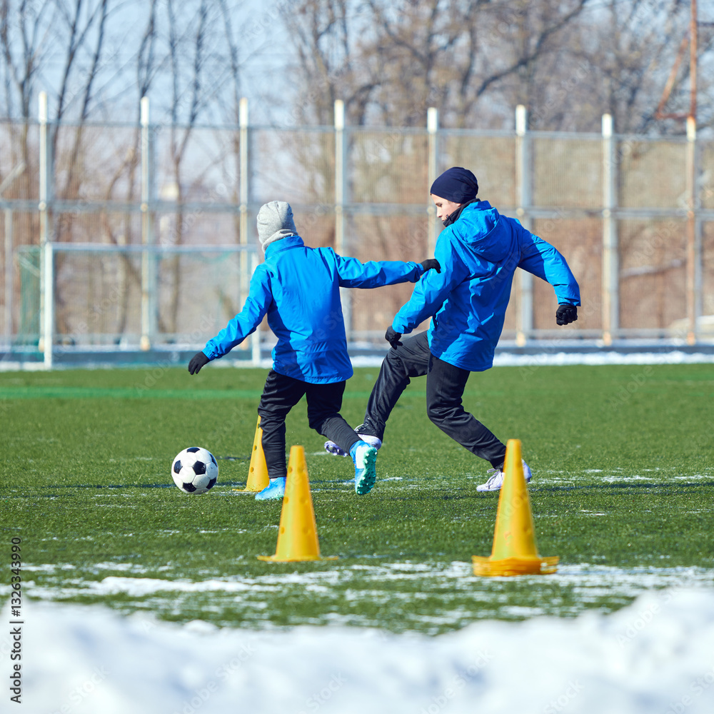 Obraz premium Youth players reacting quickly, improving decision-making and ball control on snowy green field. Focus and agility. Concept of sport, training, perseverance, dynamic movement, ambition.